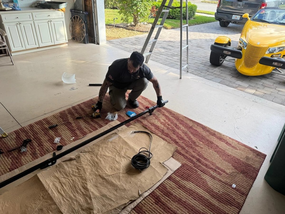 Technician kneeling on a garage floor assembling a torsion spring shaft on a drop cloth
